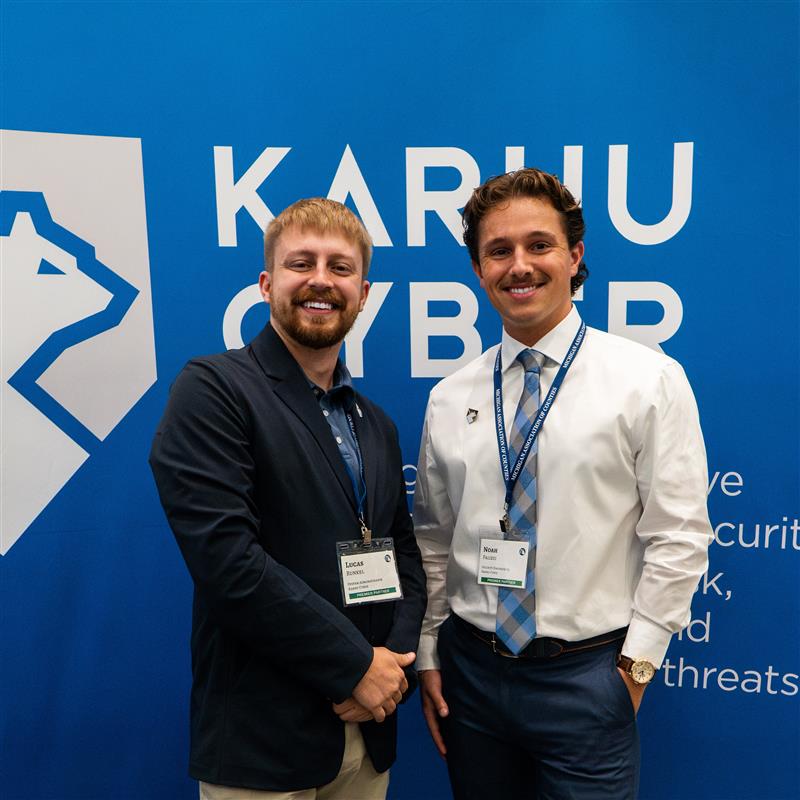 Two people standing in front of a blue Karhu Cyber display at an event