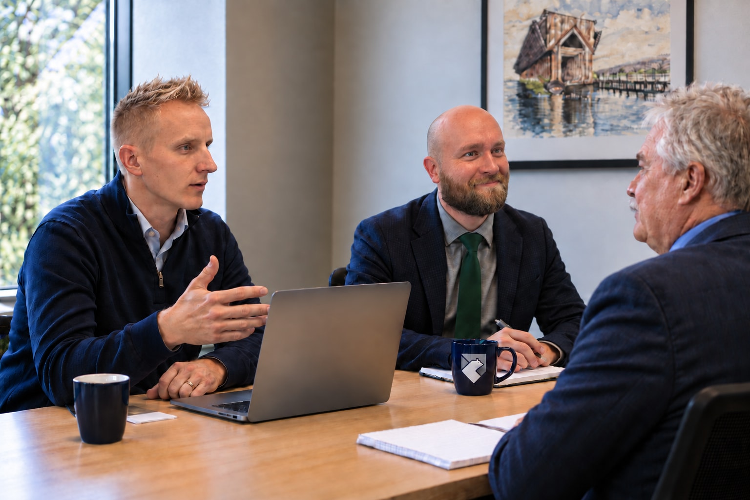 Three people discussing work around a laptop, with a Karhu-branded mug on the table